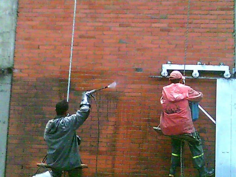 Dos operarios lavando con hidrolavadora una fachada de ladrillo